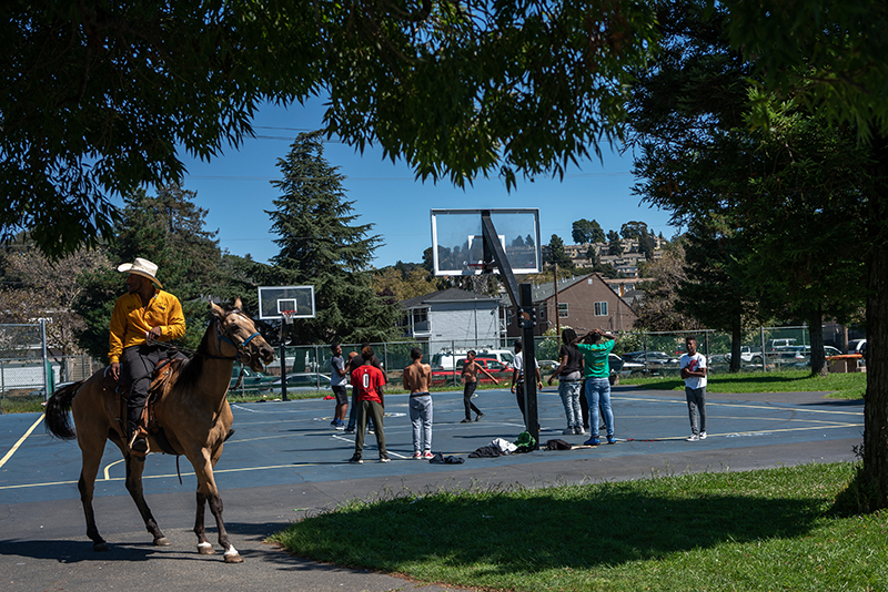 People playing basketball in background and Oakland Black Cowboy on horse in the foreground